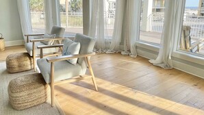 Ein Zimmer mit Holzboden, einer Couch mit Kissen und Blick auf Strand und Gebäude.