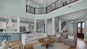 Ein großzügiger Wohnbereich mit hohen Decken, eine Küche mit weißen Schränken, eine Treppe und ein Balkon mit Geländer.