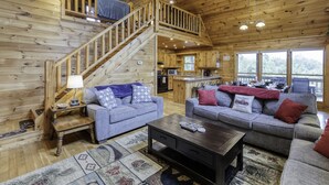 A wooden cabin interior with two sofas, a coffee table, a staircase, and a kitchen area. - Blue Ridge Cabin- Amazing Porch, Game Room, 10 Min to Town! (Blue Ridge)