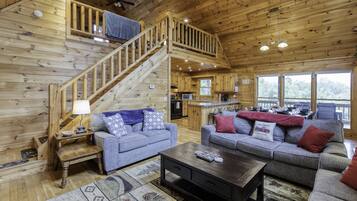 A wooden cabin interior with two sofas, a coffee table, a staircase, and a kitchen area.