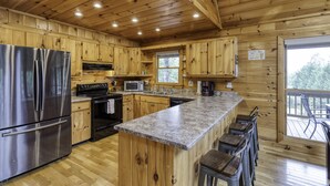 A wooden cabin kitchen with a central island, stainless steel refrigerator, microwave, and a large window overlooking the outdoors. - Blue Ridge Cabin- Amazing Porch, Game Room, 10 Min to Town! (Blue Ridge)