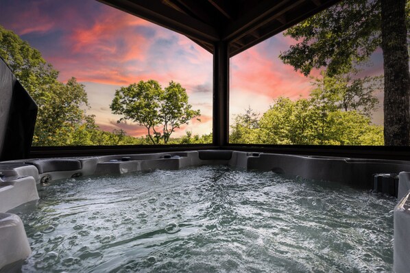 A hot tub area with a view of trees and a sunset through a wooden structure.