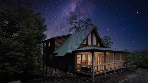 A wooden cabin with a large deck and a covered porch, surrounded by trees and a starry night sky. - Blue Ridge Cabin- Amazing Porch, Game Room, 10 Min to Town! (Blue Ridge)