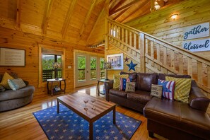 A wooden interior with a staircase, a brown leather sofa, a coffee table with two martini glasses, and a blue star-patterned rug. - Luxury Mountain Getaway 5 Minutes from Pigeon Forge Parkway! (Pigeon Forge)