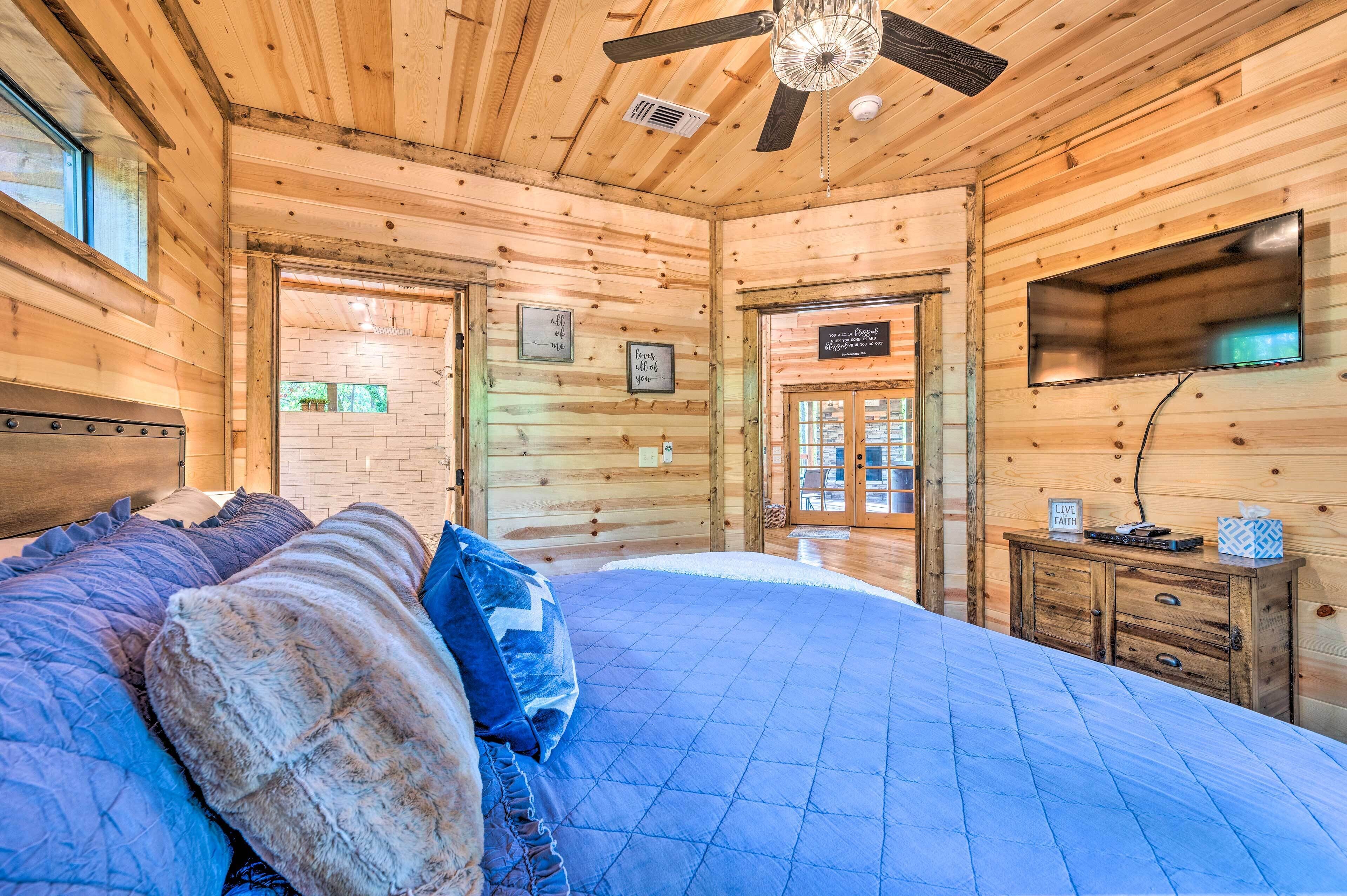 Ein Schlafzimmer in einer Blockhütte mit einem Bett, einem Deckenventilator, einem Fernseher und einer Tür, die nach draußen führt.