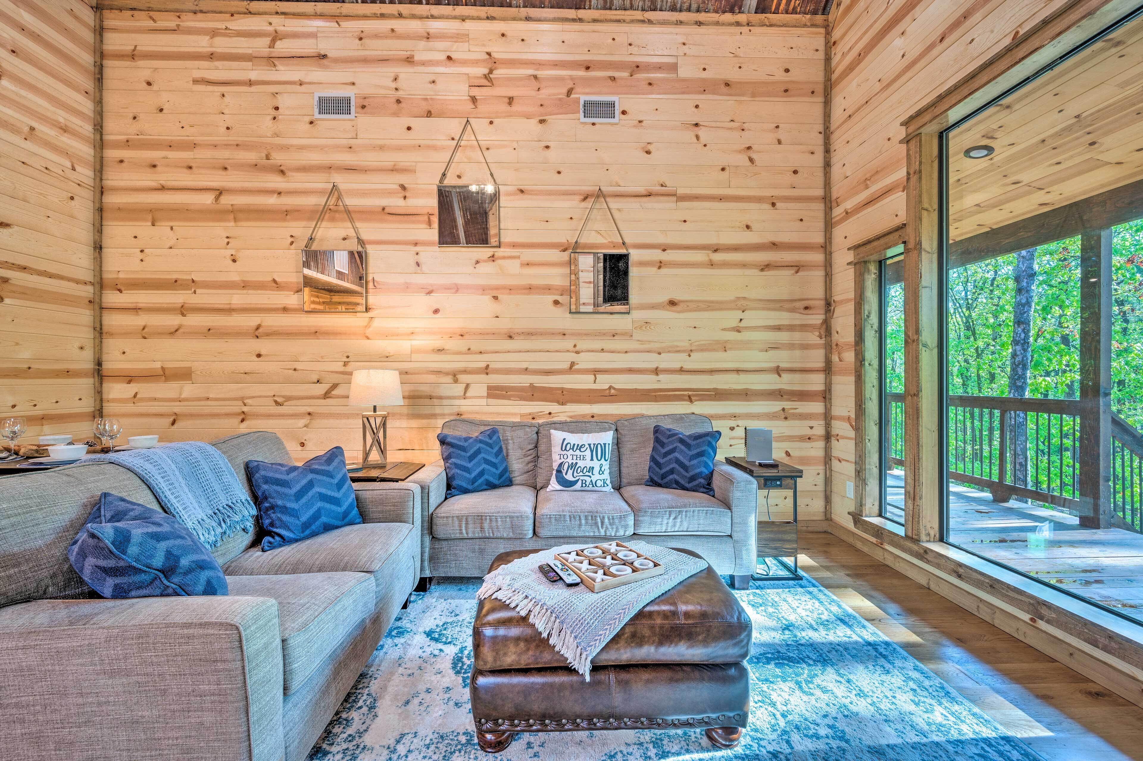 A cozy cabin interior with a wooden wall, a sofa, a loveseat, and a coffee table.