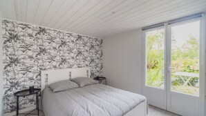 Een slaapkamer met een bed, nachtkastje en een raam met uitzicht op groen.