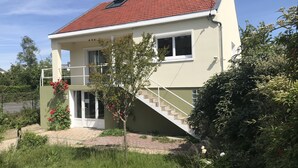 Een huis met twee verdiepingen, voorzien van een rode dakbedekking, een balkon en een trap naar de bovenverdieping.