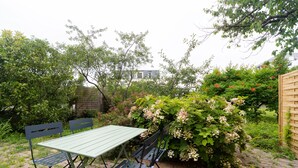 An outdoor seating area with a table and chairs, surrounded by lush greenery and flowering plants.