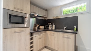 A modern kitchen with wooden cabinets, a built-in microwave, a coffee maker, and a window with a view of greenery.