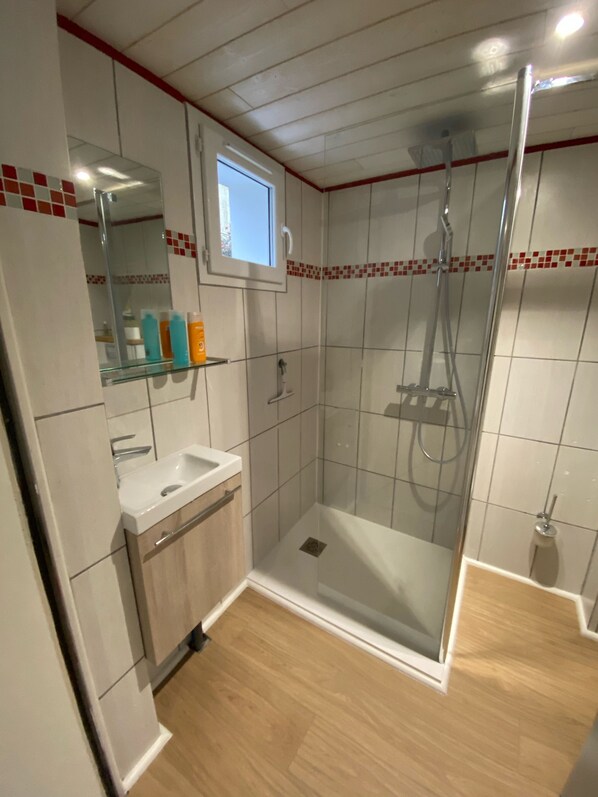 A modern bathroom with a glass shower enclosure, a sink with a mirror, and a small window above the mirror.