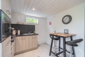 Een moderne keuken met houten kastjes, een zwart aanrecht, een spoelbak en een inbouwoven. Er is een raam boven de spoelbak en een klok aan de muur.