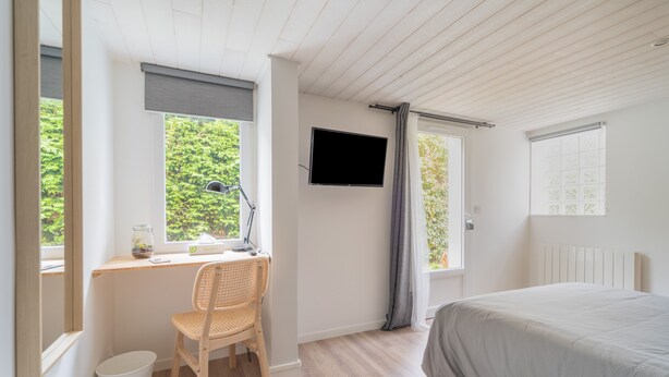 A bedroom with a bed, a desk with a chair, a TV, and windows with curtains.