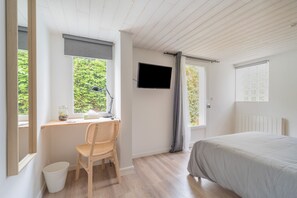 A bedroom with a bed, a desk with a chair, a TV, and windows with curtains.