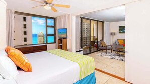 Een hotelkamer met een bed, een televisie, een balkon met uitzicht op de oceaan en een zithoek.