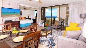 Een hotelkamer met balkon, televisie, eethoek en een bank.