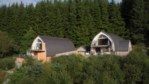 Two wooden cabins with pitched roofs, surrounded by dense forest.