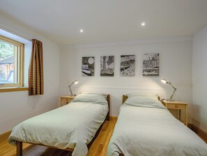 A bedroom with two single beds, a window with curtains, and three wall-mounted artworks.