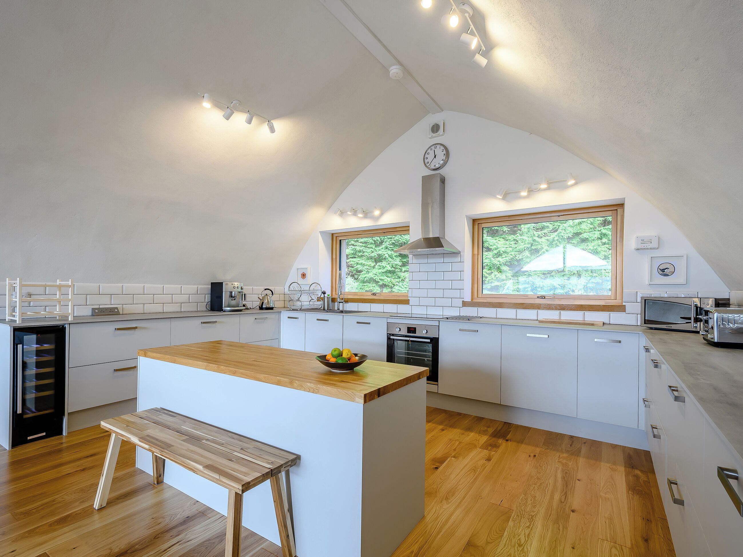 A modern kitchen with white cabinets, a wooden island, and a bench.