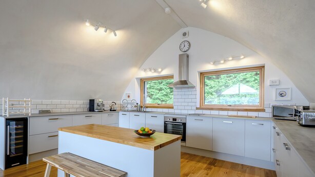 A modern kitchen with white cabinets, a wooden island, and a bench.