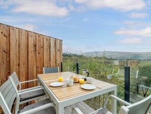 A wooden deck with a table set for breakfast, overlooking a scenic landscape.