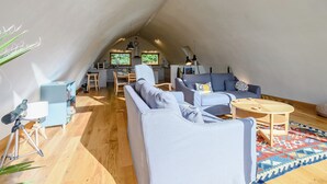 A loft-style living space with a kitchen, a sofa, a coffee table, and a tripod with a camera.
