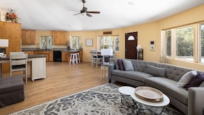 A spacious living area with a grey sofa, a dining table, and a kitchen in the background.
