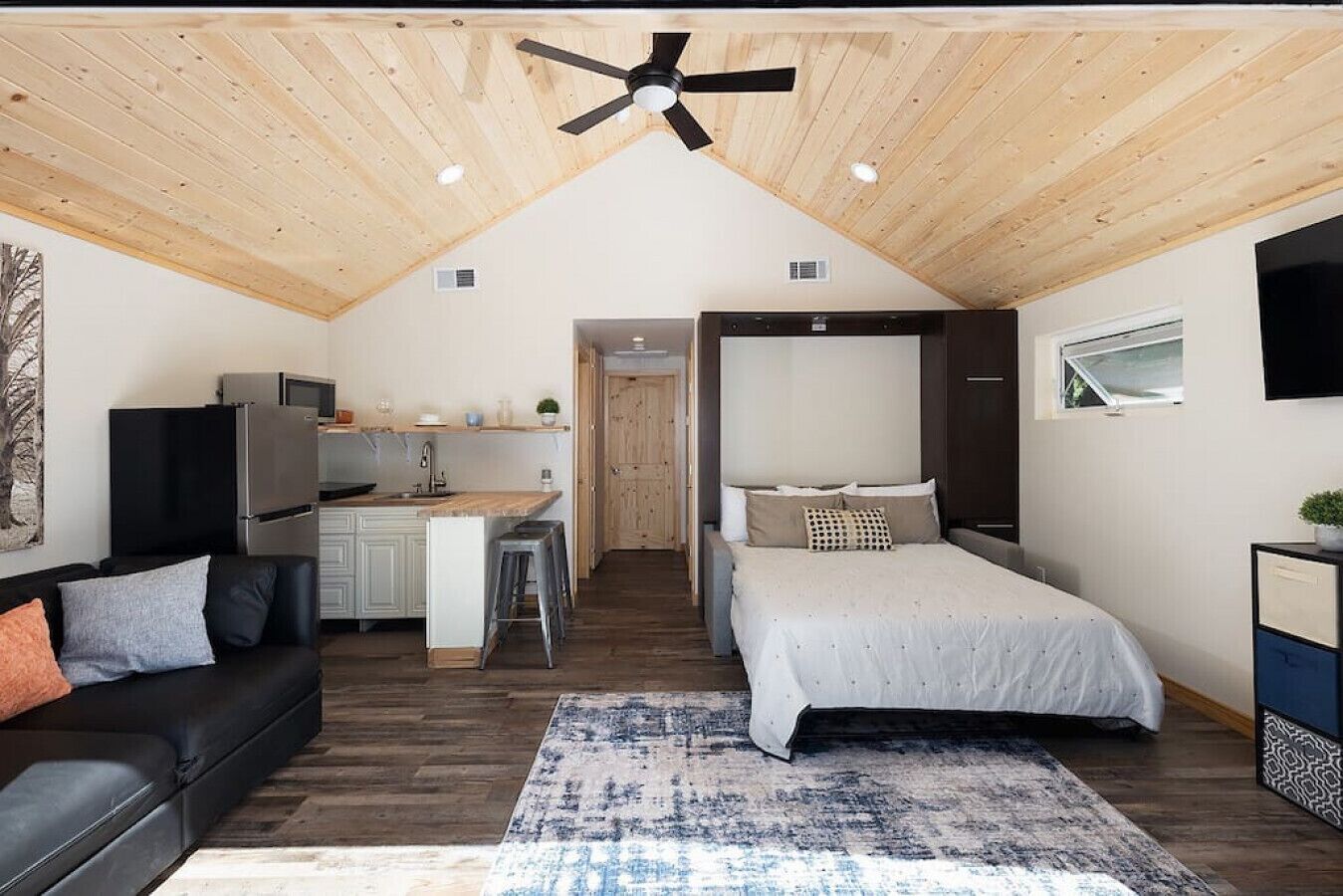 Un apartamento moderno y compacto con techo estilo loft, kitchenette, cama con cabecera, sofá y zona de comedor.