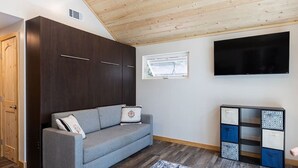 A modern living room with a grey sofa, dark wooden wardrobe, a flat-screen TV, and a patterned storage unit.