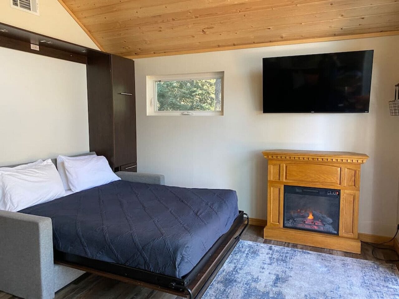 A bedroom with a bed, a television mounted on the wall, and a fireplace.