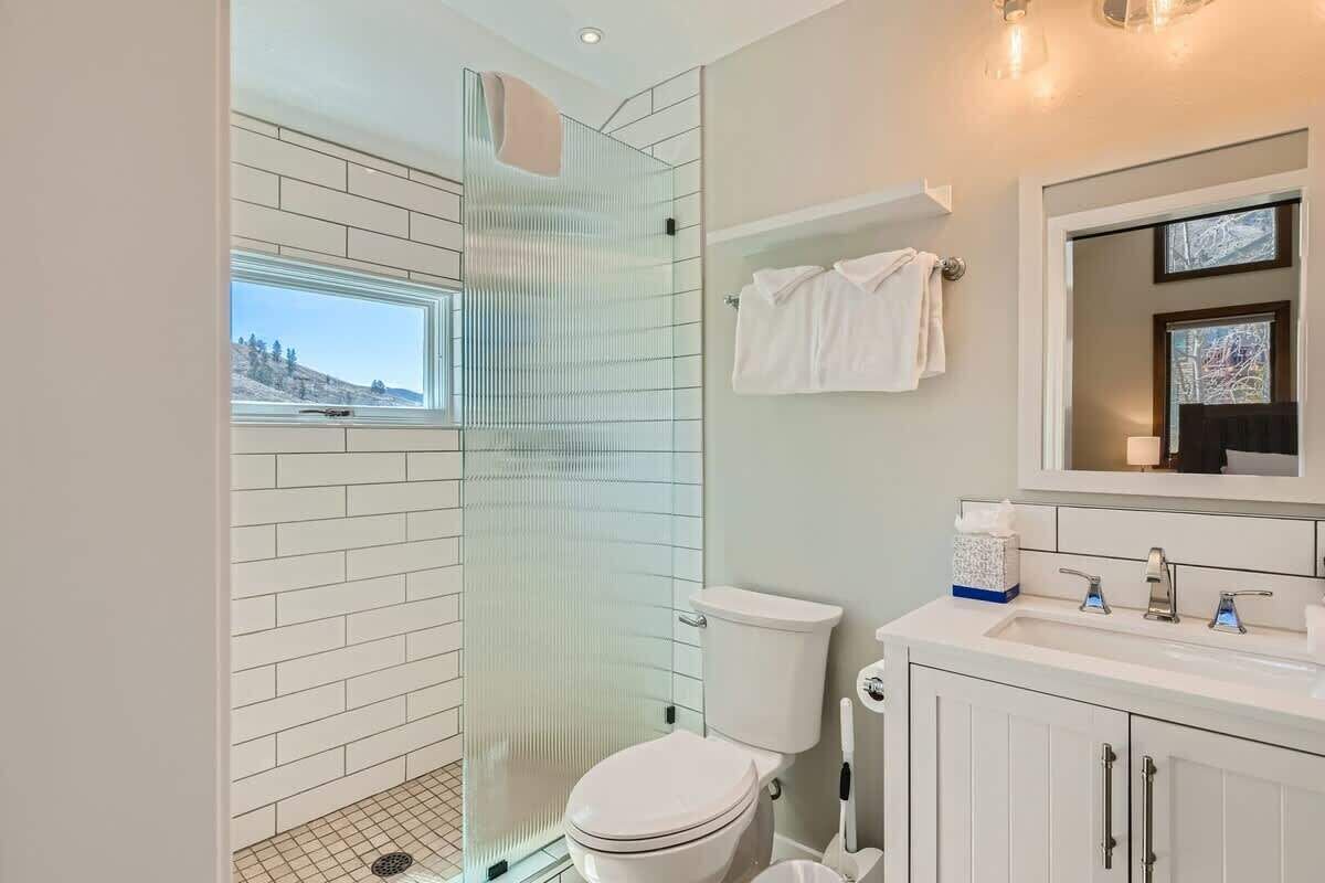 Un baño moderno con cabina de ducha de vidrio, inodoro blanco y tocador con espejo.