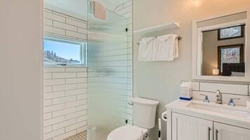 Un baño moderno con cabina de ducha de vidrio, inodoro blanco y tocador con espejo.