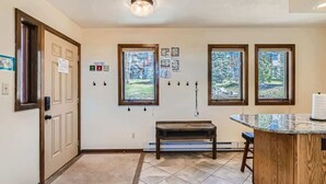 A hallway with a wooden bench, a door, and three windows with a view of trees.