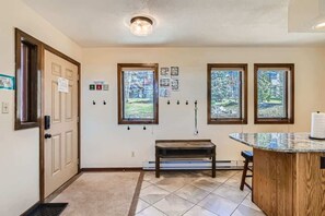 A hallway with a wooden bench, a door, and three windows with a view of trees.