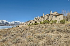 A row of beige multi-story houses with chimneys, set against a backdrop of mountains and a clear blue sky. - Family 2bedroom with Loft, Lake Views, Amazing Location (Dillon)