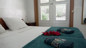 Hotellihuone, jossa on sänky, yöpöytä, lamppu ja ikkuna, jossa on sälekaihtimet.