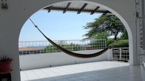 A hammock under a white archway with a view of a tiled patio and a railing.