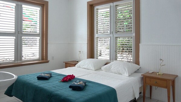 A bedroom with a bed, two nightstands, a bedside table, and a window with blinds.