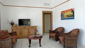 A living room with wicker furniture, a television, and a painting on the wall.