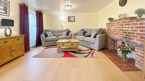 A living room with two grey sofas, a wooden coffee table, a red and grey rug, a brick fireplace, and a wooden cabinet. - 2 bedroom accommodation in Winchester (Winchester)