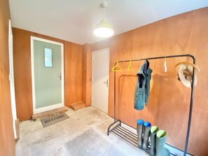A room with a wooden wall, a coat rack with hangers, a door, and a welcome mat.
