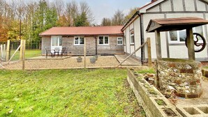 A rustic wooden house with a red-tiled roof, a fenced patio with outdoor furniture, and a stone well. - 2 bedroom accommodation in Winchester (Winchester)