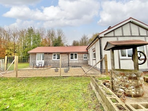 A rustic wooden house with a red-tiled roof, a fenced patio with outdoor furniture, and a stone well. - 2 bedroom accommodation in Winchester (Winchester)