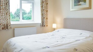 A bedroom with a bed, a window with floral curtains, a radiator, and a framed picture on the wall.