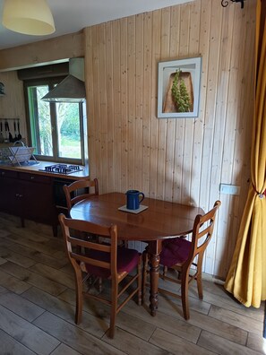 A wooden-paneled room with a dining table, chairs, a blue mug, and a framed picture on the wall.