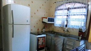 A compact kitchen with a refrigerator, stove, microwave, and a window with lace curtains. - Vacation Home in Praia Grande - 3 min. Beach (Praia Grande)