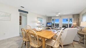 A spacious living room with a dining area, a television, and a view of the ocean. - Needle Rush Point C14 | Walk to FloraBama | Beachfront | My Beach Getaways (Pensacola)