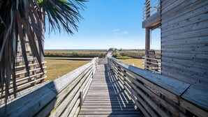 A wooden boardwalk leading to a beach with a wooden building on the right. - Needle Rush Point C14 | Walk to FloraBama | Beachfront | My Beach Getaways (Pensacola)