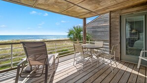 Una terraza de madera con una mesa y sillas, con vista a una playa.