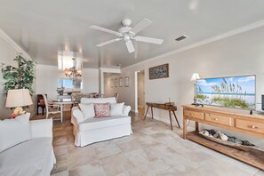 Un salon spacieux doté d’un ventilateur de plafond, un coin repas agrémenté d’un lustre, et un grand téléviseur fixé au mur.